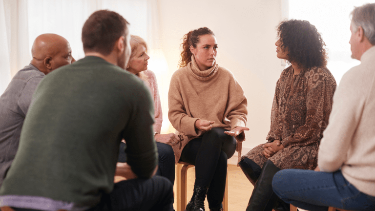 A group of diverse people sit in a circle, in a support group formation