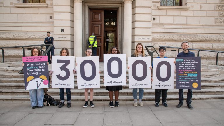 A group of people stands with banners outside the Treasury